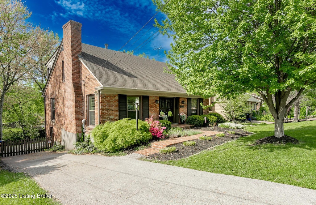 view of front of house featuring a chimney, a shingled roof, fence, a front lawn, and brick siding