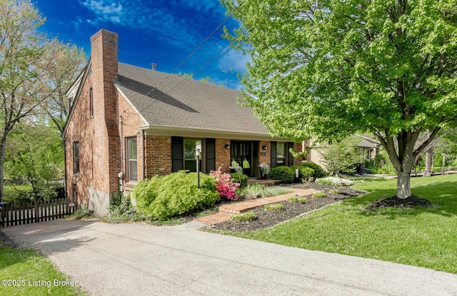 view of front of house featuring a chimney, a shingled roof, fence, a front lawn, and brick siding