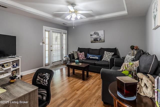 living area with ceiling fan, visible vents, a tray ceiling, baseboards, and light wood-type flooring