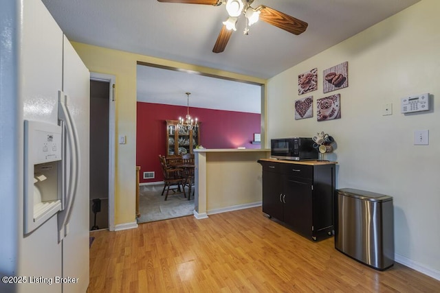 kitchen with black microwave, white refrigerator with ice dispenser, dark cabinetry, light wood finished floors, and ceiling fan with notable chandelier
