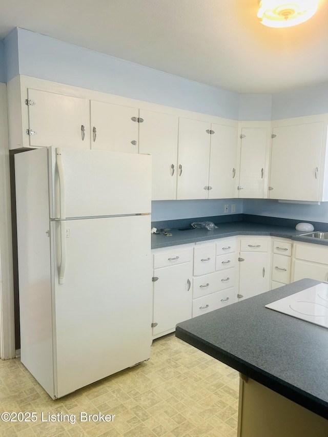 kitchen featuring white appliances, light floors, dark countertops, a sink, and white cabinetry