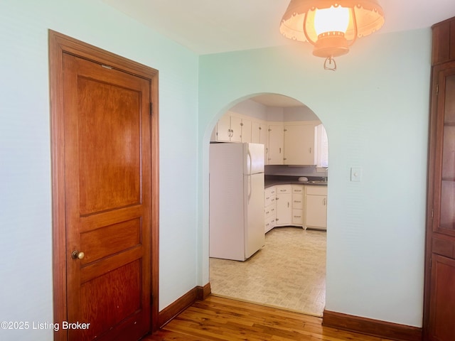 corridor with baseboards, wood finished floors, arched walkways, and a sink