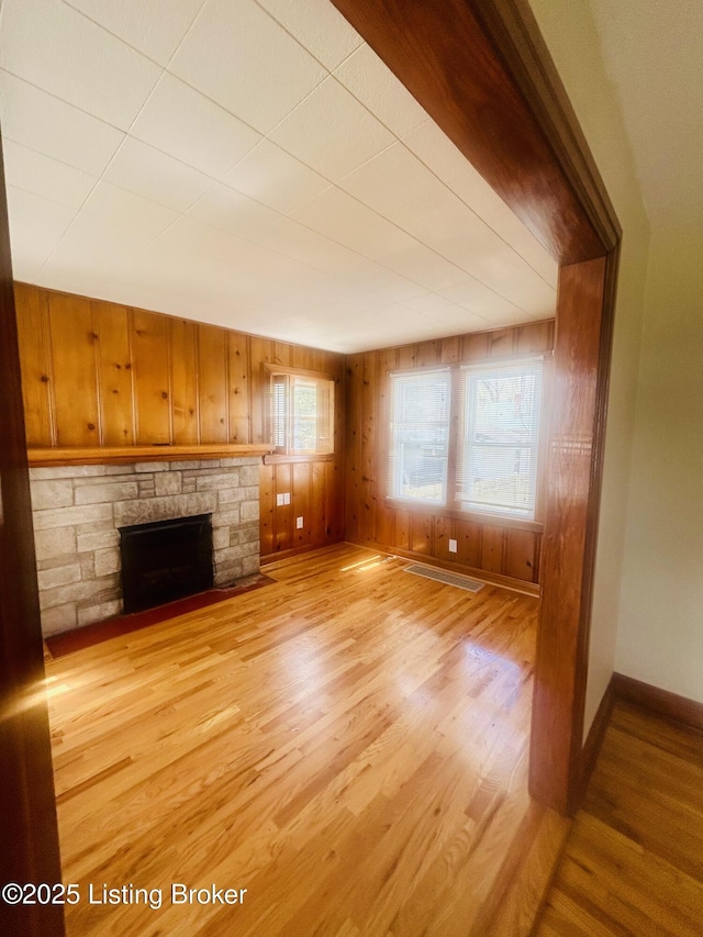 unfurnished living room with baseboards, wood walls, a stone fireplace, and light wood finished floors