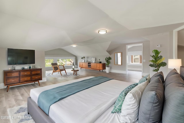 bedroom with baseboards, light wood-style floors, and vaulted ceiling