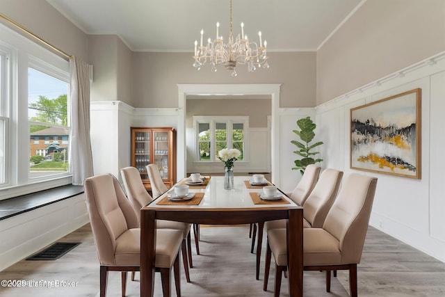 dining room featuring an inviting chandelier, a decorative wall, ornamental molding, light wood finished floors, and visible vents