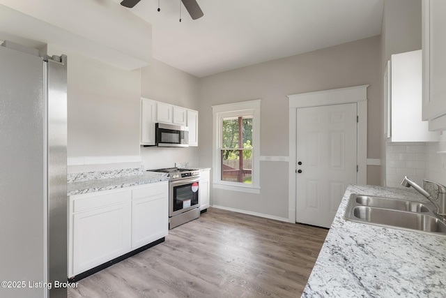 kitchen featuring a sink, stainless steel appliances, ceiling fan, white cabinetry, and light countertops