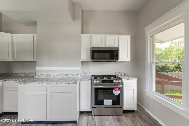 kitchen featuring light wood-style flooring, light stone counters, appliances with stainless steel finishes, and white cabinetry