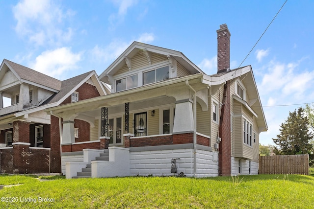 view of front of home with a chimney, a porch, brick siding, fence, and a front yard