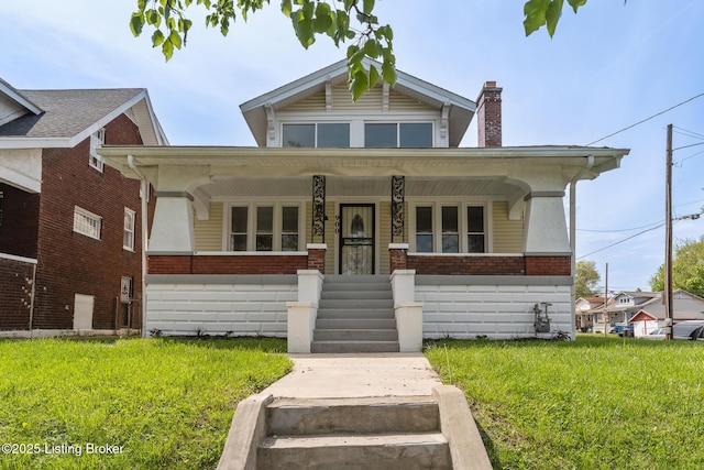 bungalow-style house with a front yard, a chimney, covered porch, and brick siding