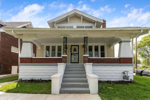 bungalow-style home featuring a chimney, brick siding, and a porch