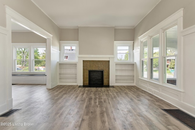 unfurnished living room featuring wood finished floors, visible vents, a tiled fireplace, and crown molding