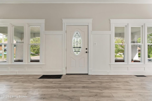 foyer entrance featuring visible vents, a decorative wall, and light wood-style floors