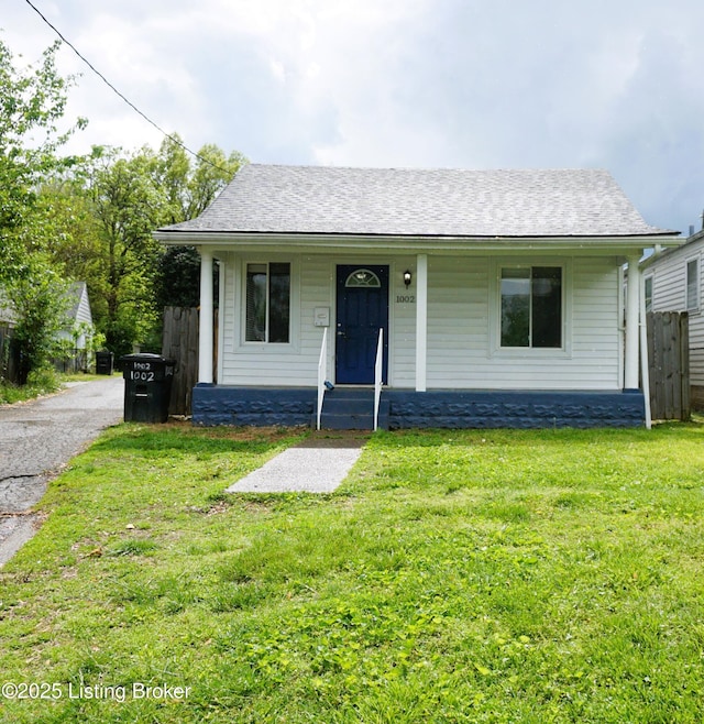 view of front of home with fence, roof with shingles, covered porch, and a front lawn