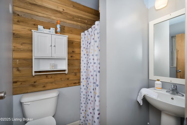 bathroom with a sink, curtained shower, wood walls, and toilet