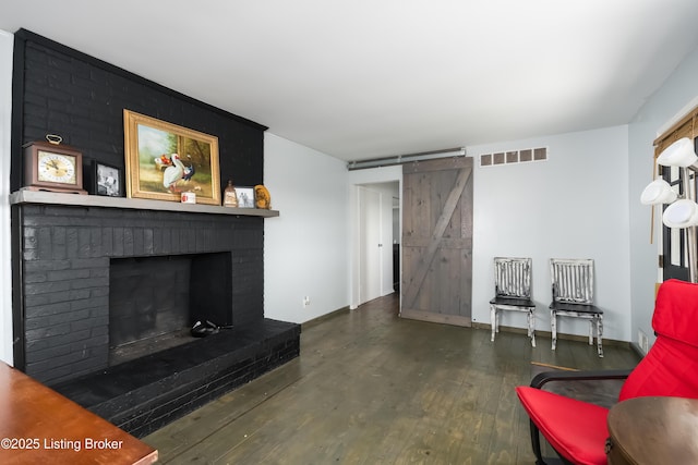 living area with visible vents, a brick fireplace, wood finished floors, baseboards, and a barn door