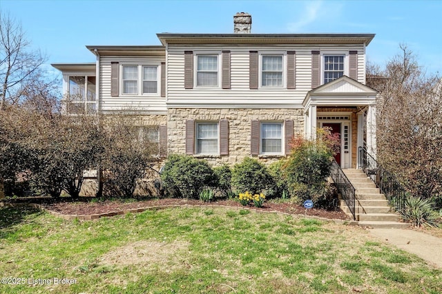 view of front facade featuring a front lawn, stone siding, a sunroom, and a chimney