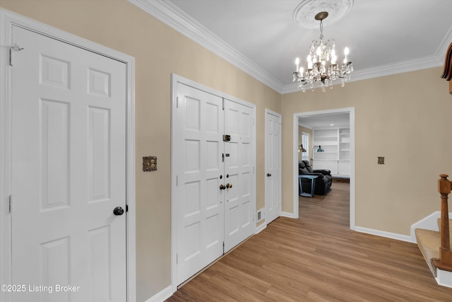 foyer entrance featuring baseboards, light wood finished floors, ornamental molding, a notable chandelier, and stairs