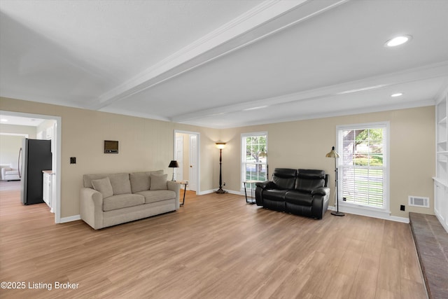 living area featuring baseboards, a wealth of natural light, light wood finished floors, beam ceiling, and visible vents