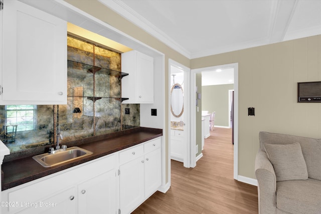kitchen featuring white cabinets, light wood-style flooring, a sink, dark countertops, and ornamental molding