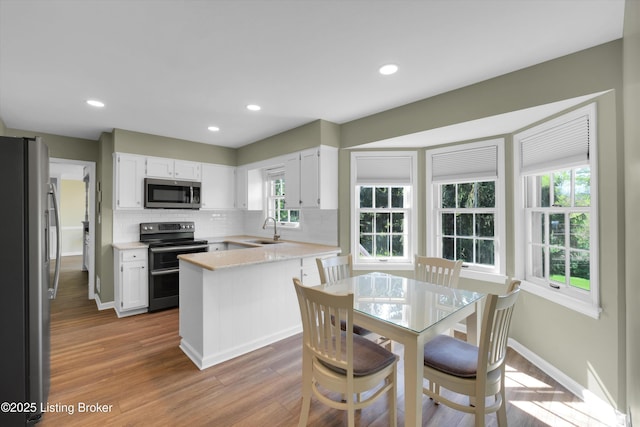 kitchen featuring wood finished floors, decorative backsplash, appliances with stainless steel finishes, white cabinets, and a sink