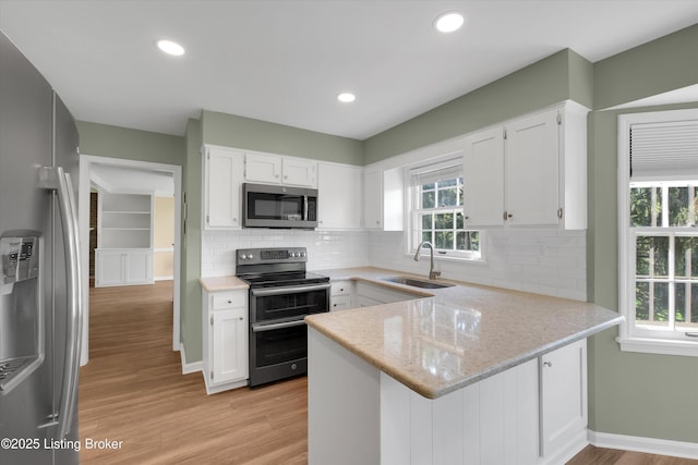 kitchen with appliances with stainless steel finishes, a peninsula, white cabinets, and a sink