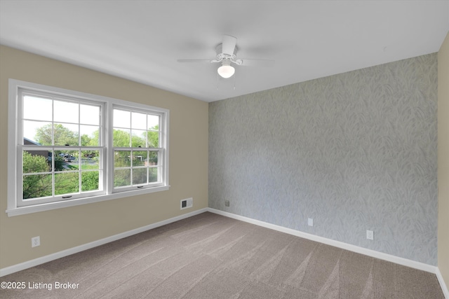 carpeted spare room featuring baseboards, visible vents, ceiling fan, and wallpapered walls