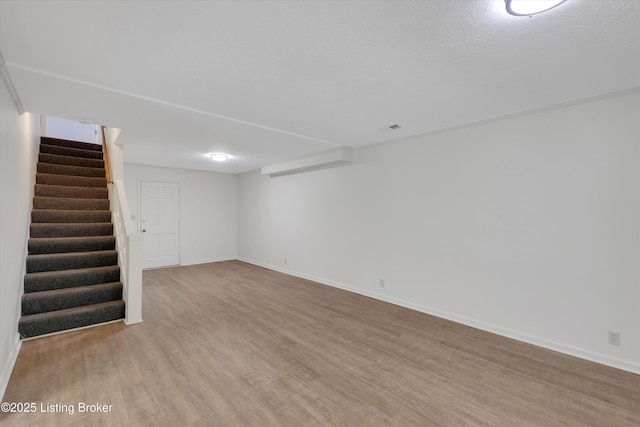 finished below grade area featuring stairway, light wood-style floors, and baseboards