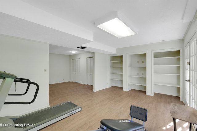 exercise area featuring built in shelves, visible vents, wood finished floors, and baseboards