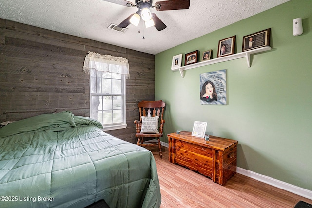 bedroom featuring a textured ceiling, visible vents, baseboards, wooden walls, and wood finished floors