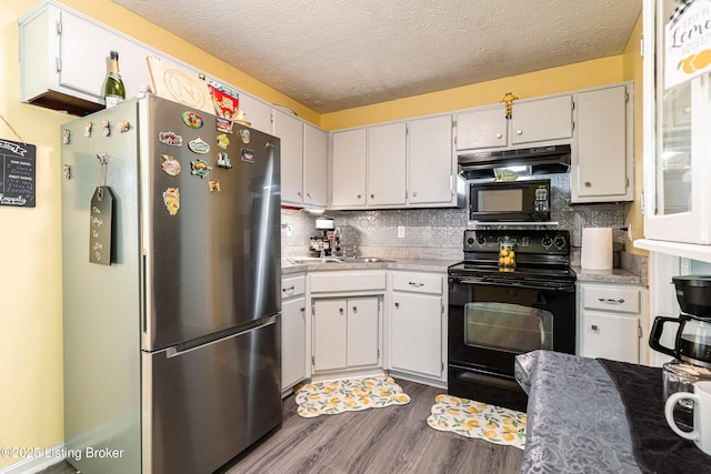 kitchen featuring a sink, under cabinet range hood, black appliances, dark wood-type flooring, and backsplash