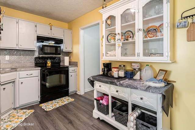 kitchen featuring tasteful backsplash, glass insert cabinets, light countertops, black appliances, and dark wood finished floors