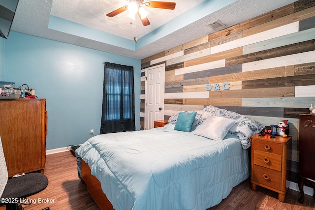 bedroom with a raised ceiling, visible vents, baseboards, wooden walls, and wood finished floors