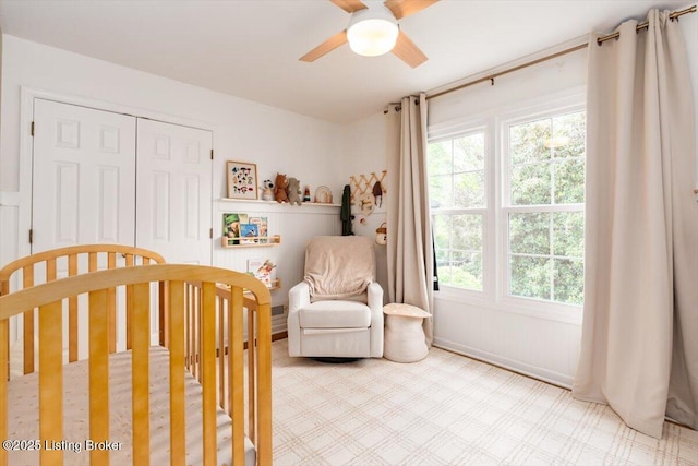 bedroom with a crib, ceiling fan, and a closet