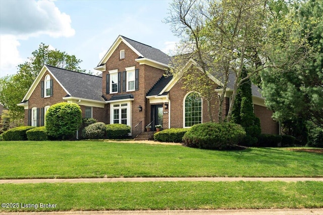 view of front of home with brick siding, a front yard, and roof with shingles