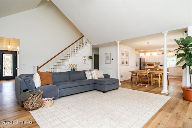 living area featuring decorative columns, light wood-style floors, high vaulted ceiling, and stairs
