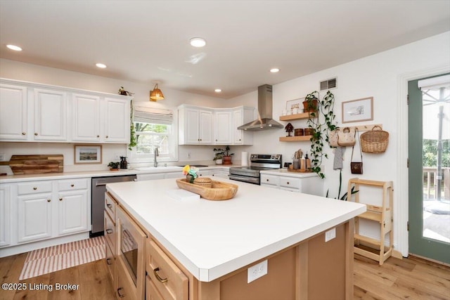 kitchen featuring light wood-style floors, wall chimney exhaust hood, visible vents, white cabinets, and appliances with stainless steel finishes