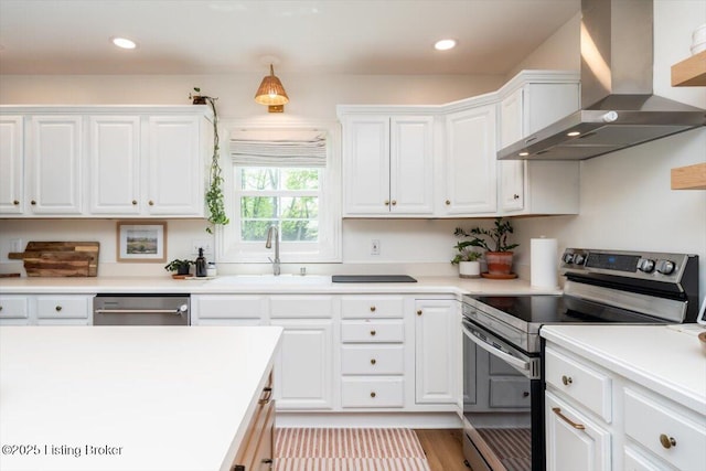 kitchen with a sink, wall chimney exhaust hood, white cabinetry, light countertops, and appliances with stainless steel finishes