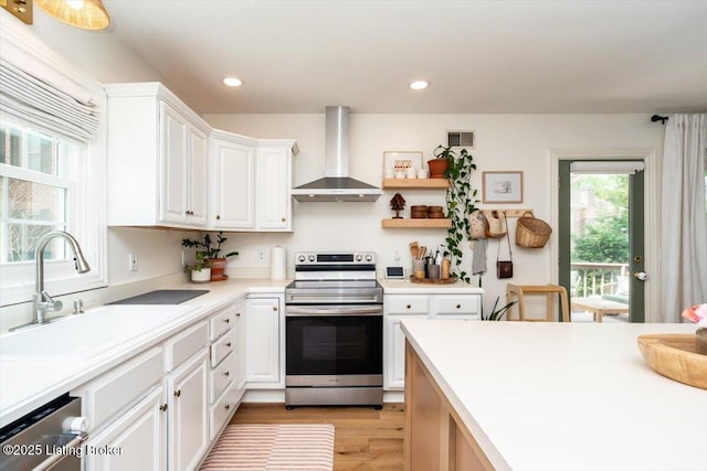 kitchen featuring appliances with stainless steel finishes, light countertops, wall chimney range hood, a sink, and visible vents