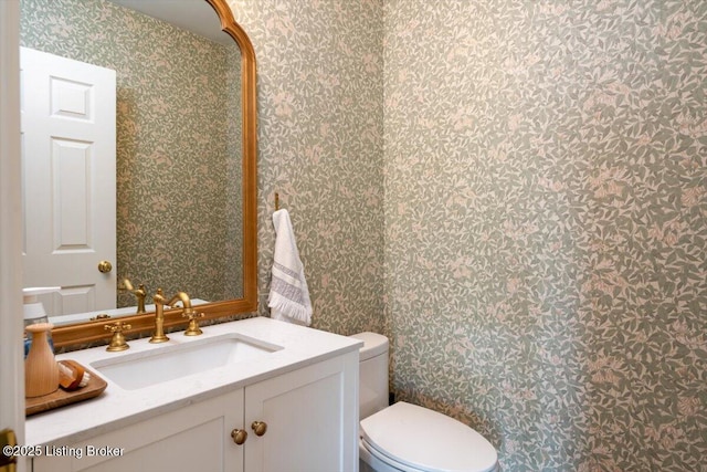 half bathroom featuring vanity, toilet, and wallpapered walls