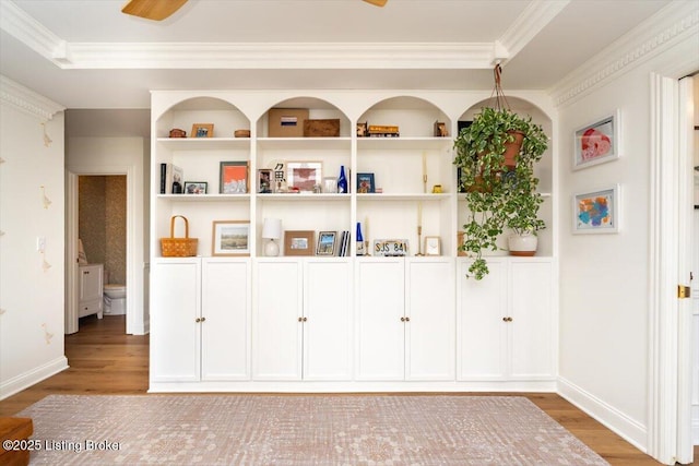 interior space featuring wood finished floors, crown molding, built in shelves, and baseboards