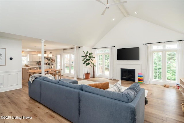 living area featuring ceiling fan, light wood-style floors, beam ceiling, a fireplace, and high vaulted ceiling