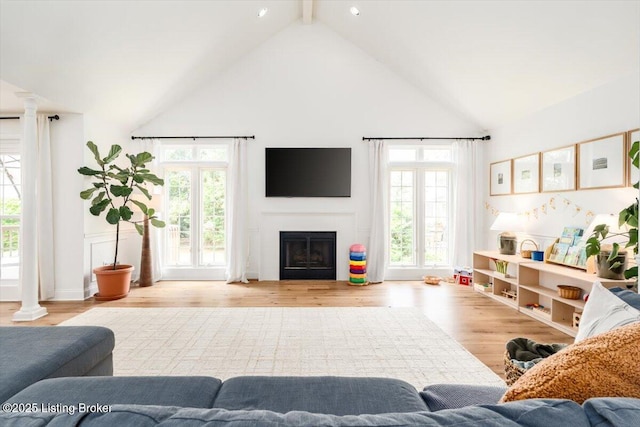 living room featuring beam ceiling, a fireplace, ornate columns, wood finished floors, and high vaulted ceiling