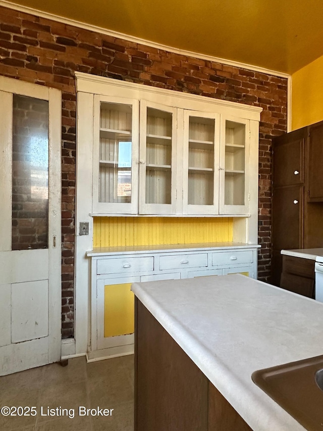 1460 S 6th St, Louisville, KY 40208 - kitchen featuring glass insert cabinets, light countertops, tile patterned floors, and brick wall