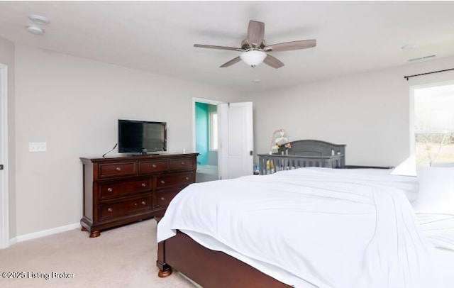 bedroom featuring ceiling fan, baseboards, light colored carpet, and ensuite bath