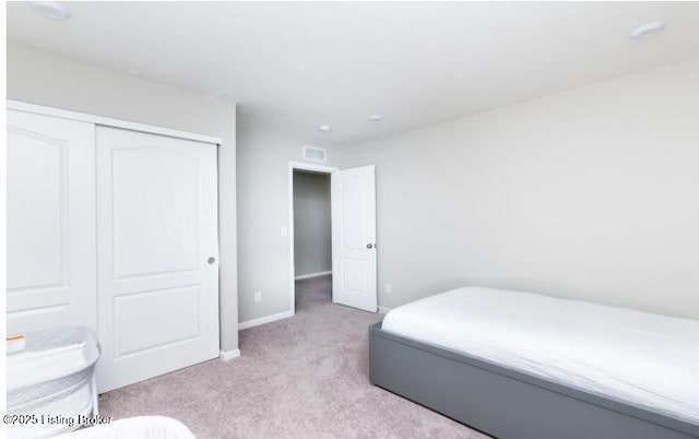 bedroom with baseboards, visible vents, a closet, and light colored carpet