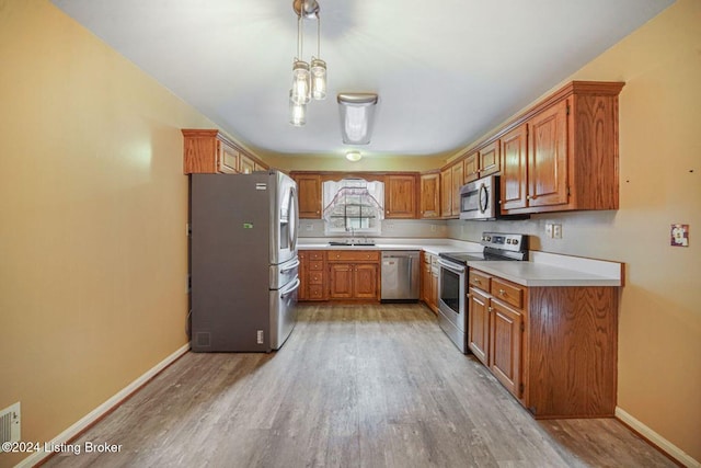 kitchen featuring light wood-style floors, brown cabinetry, baseboards, light countertops, and appliances with stainless steel finishes