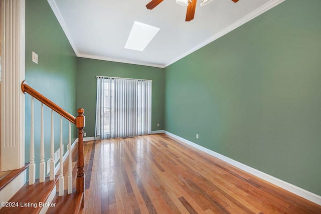 empty room featuring crown molding, hardwood / wood-style floors, baseboards, a ceiling fan, and a skylight