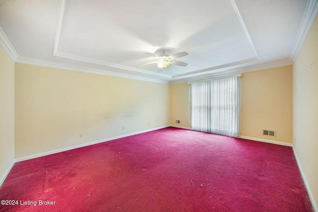 carpeted spare room with a raised ceiling, visible vents, baseboards, ornamental molding, and a ceiling fan