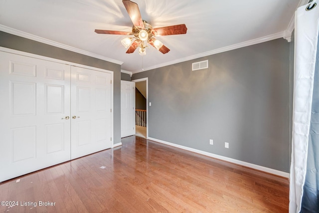 unfurnished bedroom with wood finished floors, a closet, ornamental molding, baseboards, and visible vents