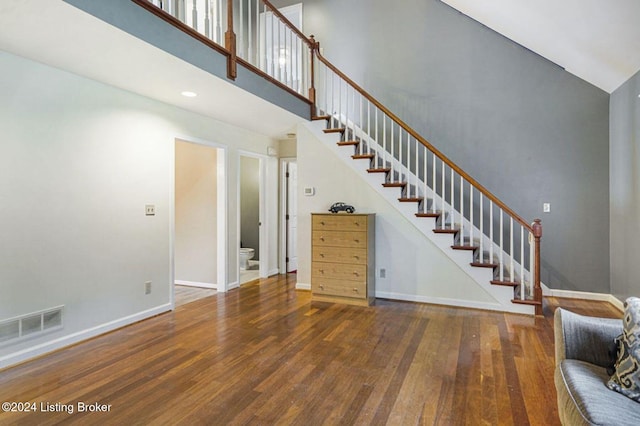 unfurnished living room featuring visible vents, wood finished floors, a high ceiling, and stairway